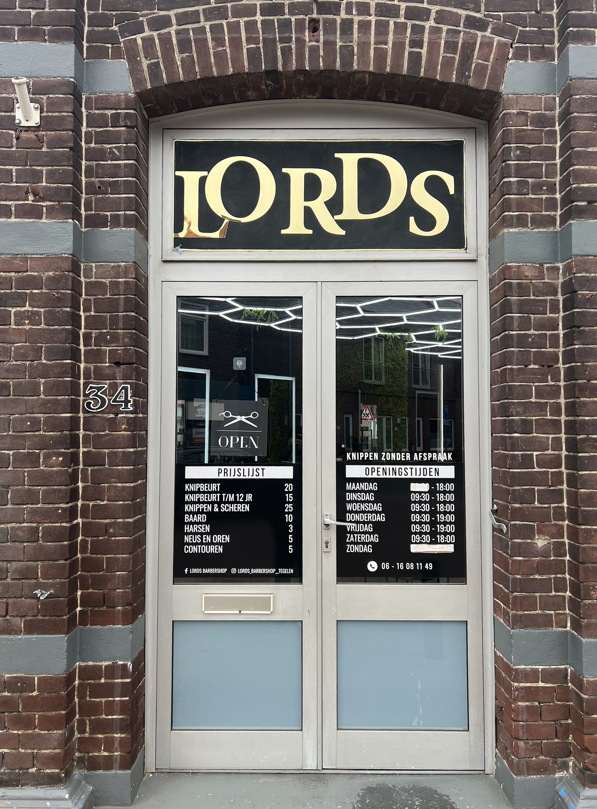 De voordeur van Lords Barbershop aan de Schoolstraat 34, met het gouden LORDS-bord boven de deur en de prijslijst en openingstijden op het glas